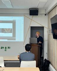 강의실에서 발표 화면 앞에 서서 강의를 진행하는 모습