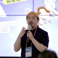 콘텐츠 화면을 배경으로 마이크 들고 발표하는 강의 장면